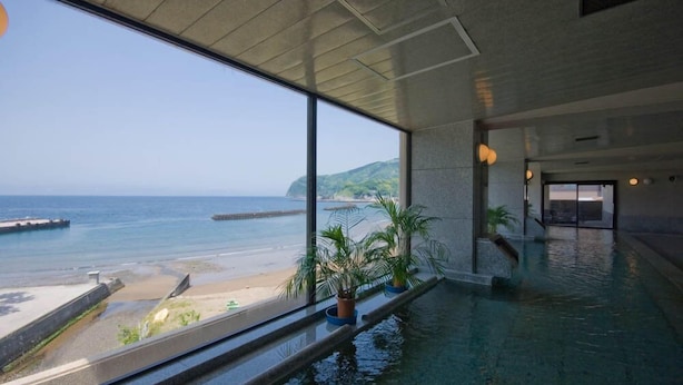 A spacious indoor area with large windows overlooking a beach and ocean. - Aoki-nagi-no-yado Meijikan (Izu)