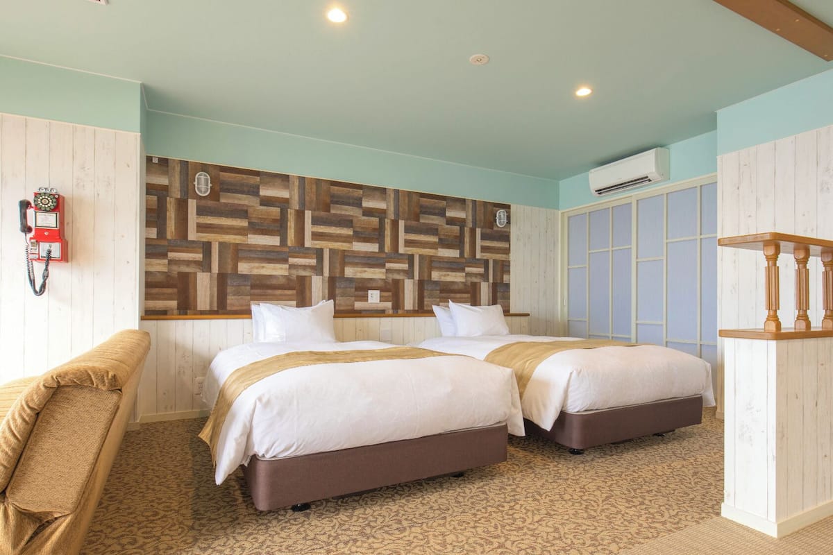 A hotel room with two beds, a wooden headboard, a small desk, and a chair.