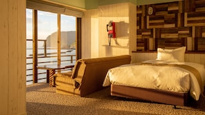 A hotel room with a large bed, a sofa, a wooden wall panel, and a view of the sea. - Aoki-nagi-no-yado Meijikan (Izu)