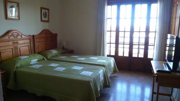 Una habitación con dos camas, cabecera de madera, un escritorio con una computadora portátil y una ventana con cortinas.