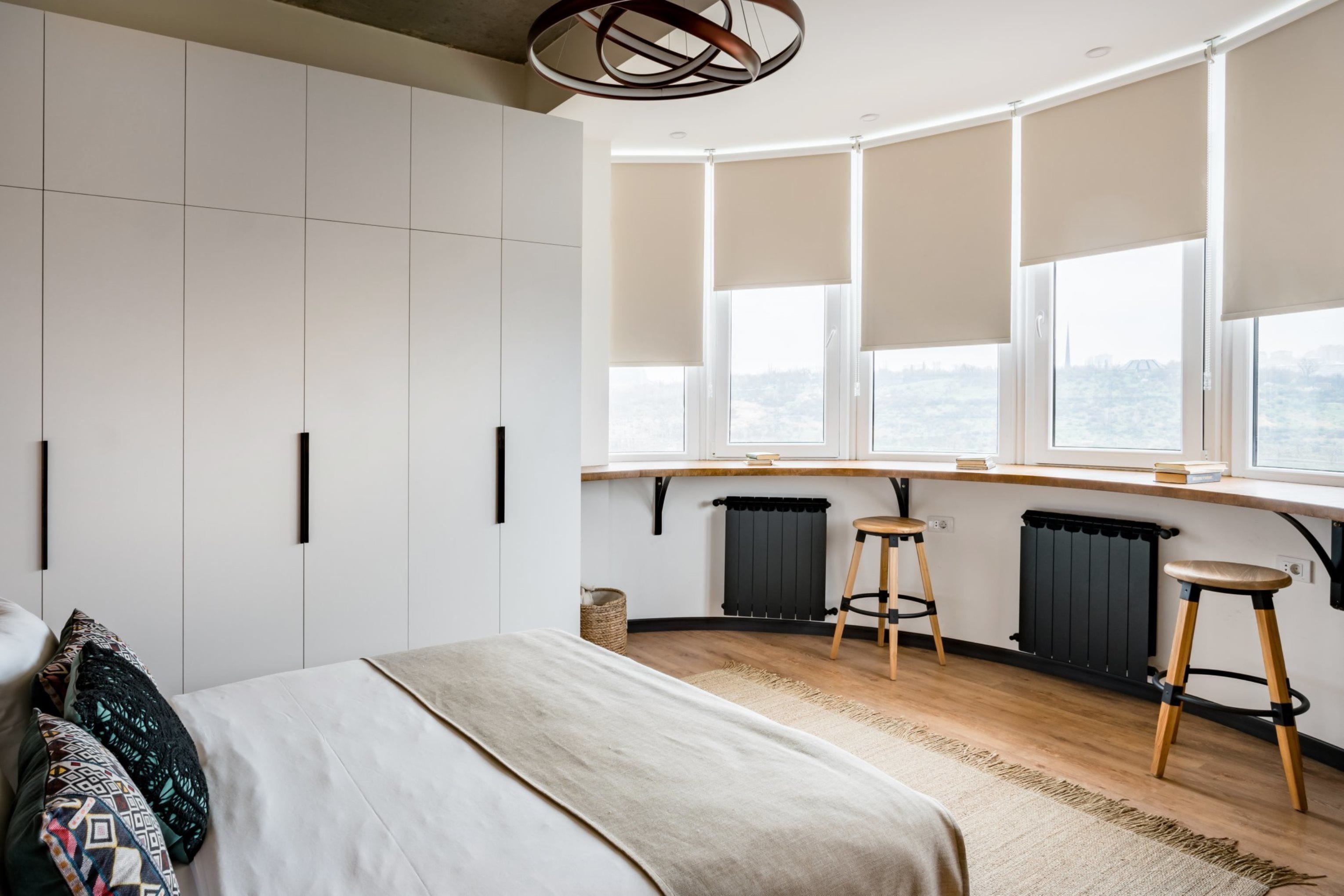 A modern bedroom with a curved window, a bed, a desk, and two stools.