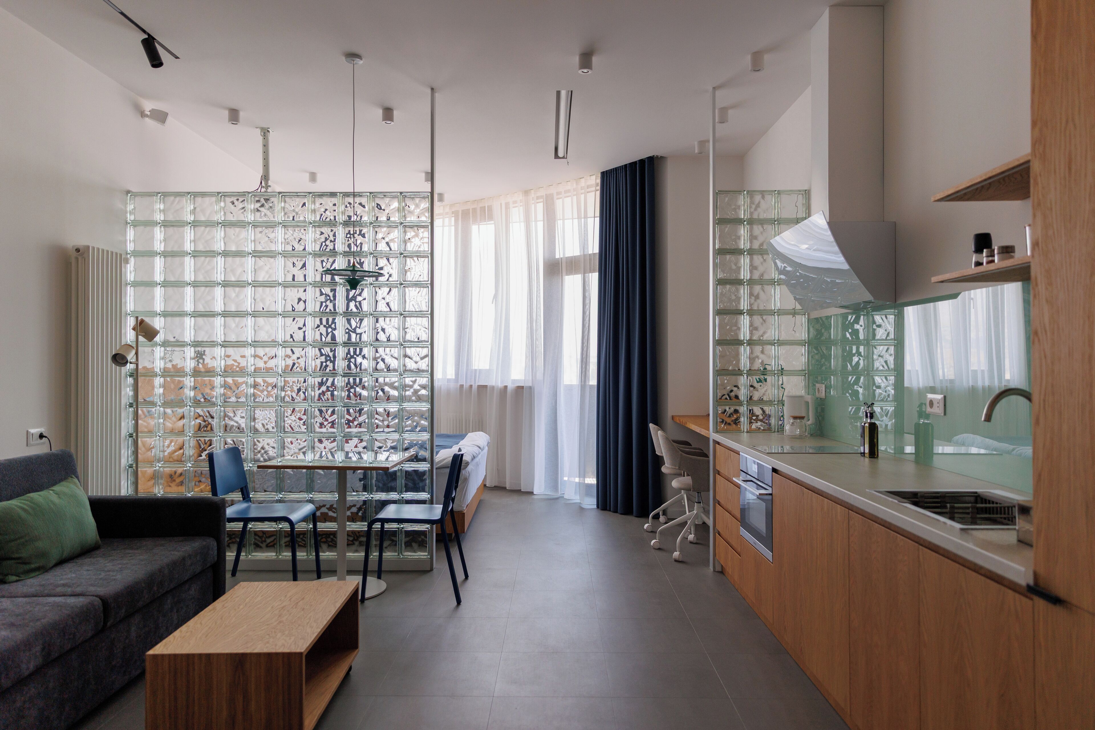 A modern kitchen with a built-in oven, a dining area with a glass partition, and a sofa with a green cushion.