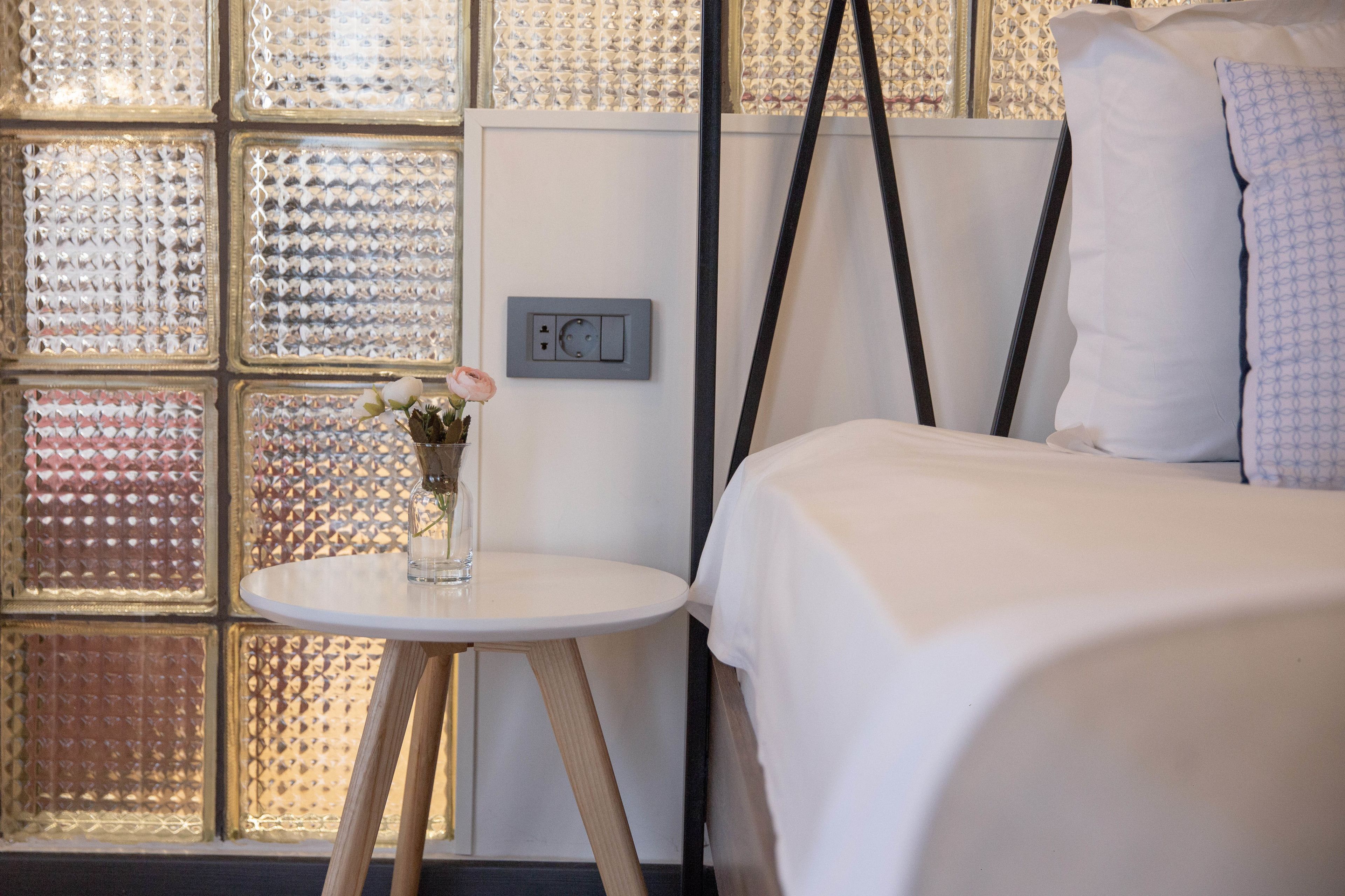 Habitación de hotel con una cama, una pequeña mesa redonda con un jarrón de flores y una pared con textura.