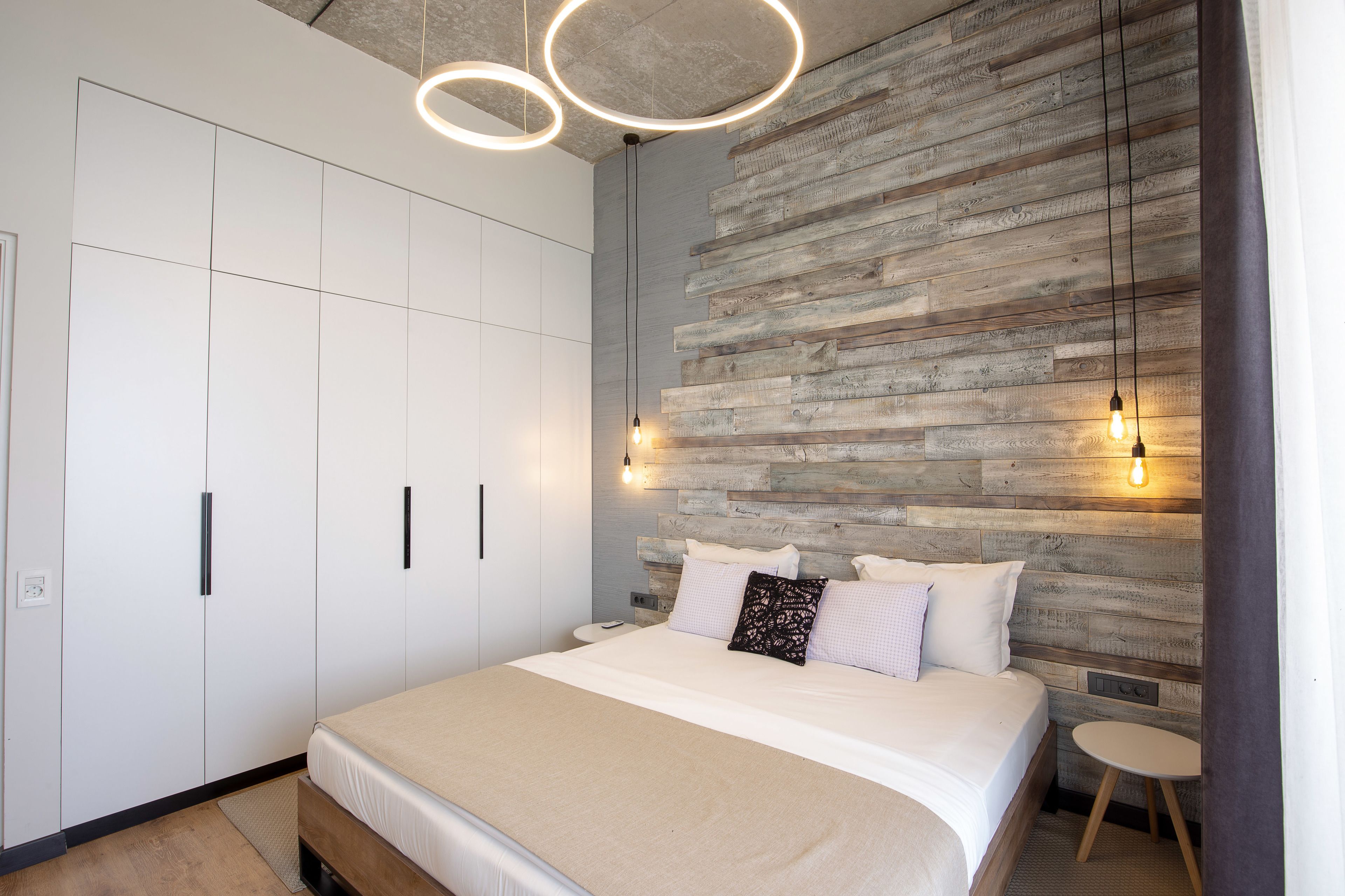 A bedroom with a bed, a wardrobe, and a wall with a wooden texture. There are two pendant lights above the bed.