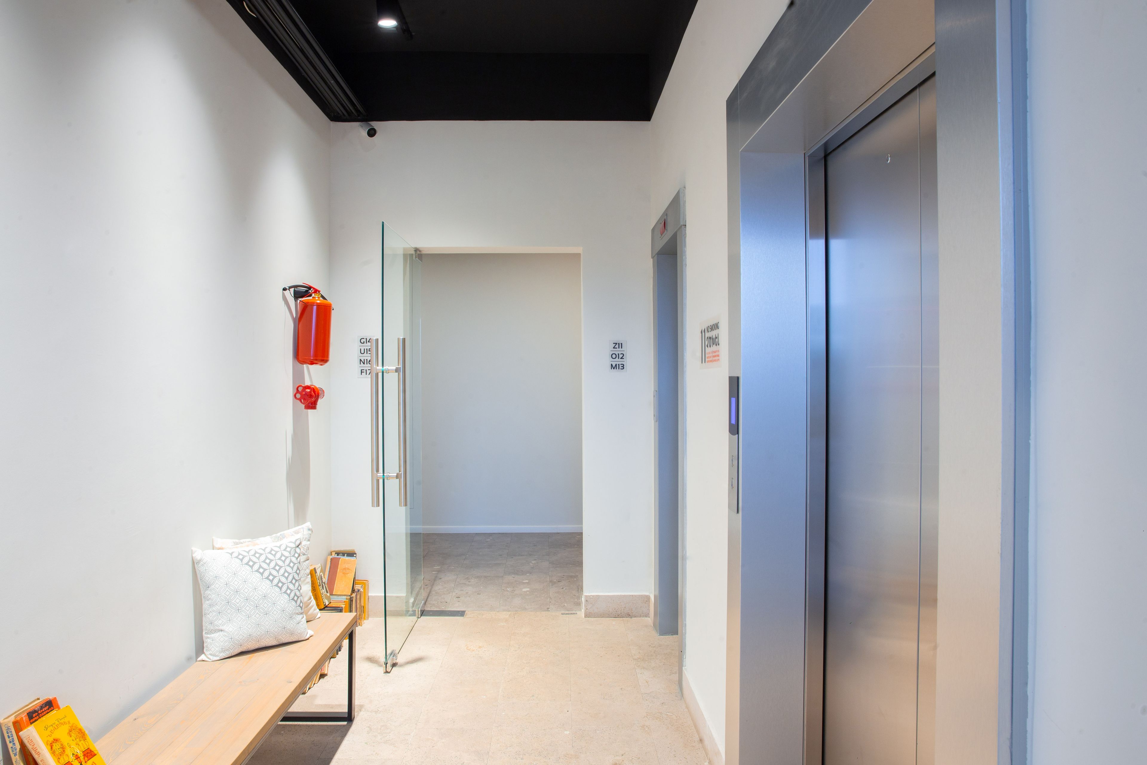 A modern hallway with a bench, a glass partition, and an elevator.