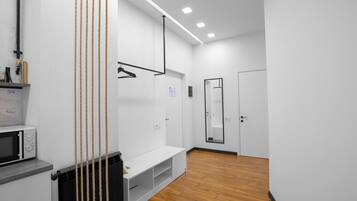 A modern, minimalist room with a white wall, a wooden floor, a white bench, a black radiator, and a white microwave.