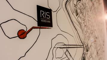 Una pared con un letrero negro que dice "RIS DALMA COLLECTION YEREVAN" y un objeto rojo parecido a una llave.