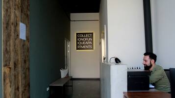 A reception area with a wooden wall, a bench, a desk with a computer, and a sign that reads "COLLECT IONOFUN IQUEAPA RTMENTS".