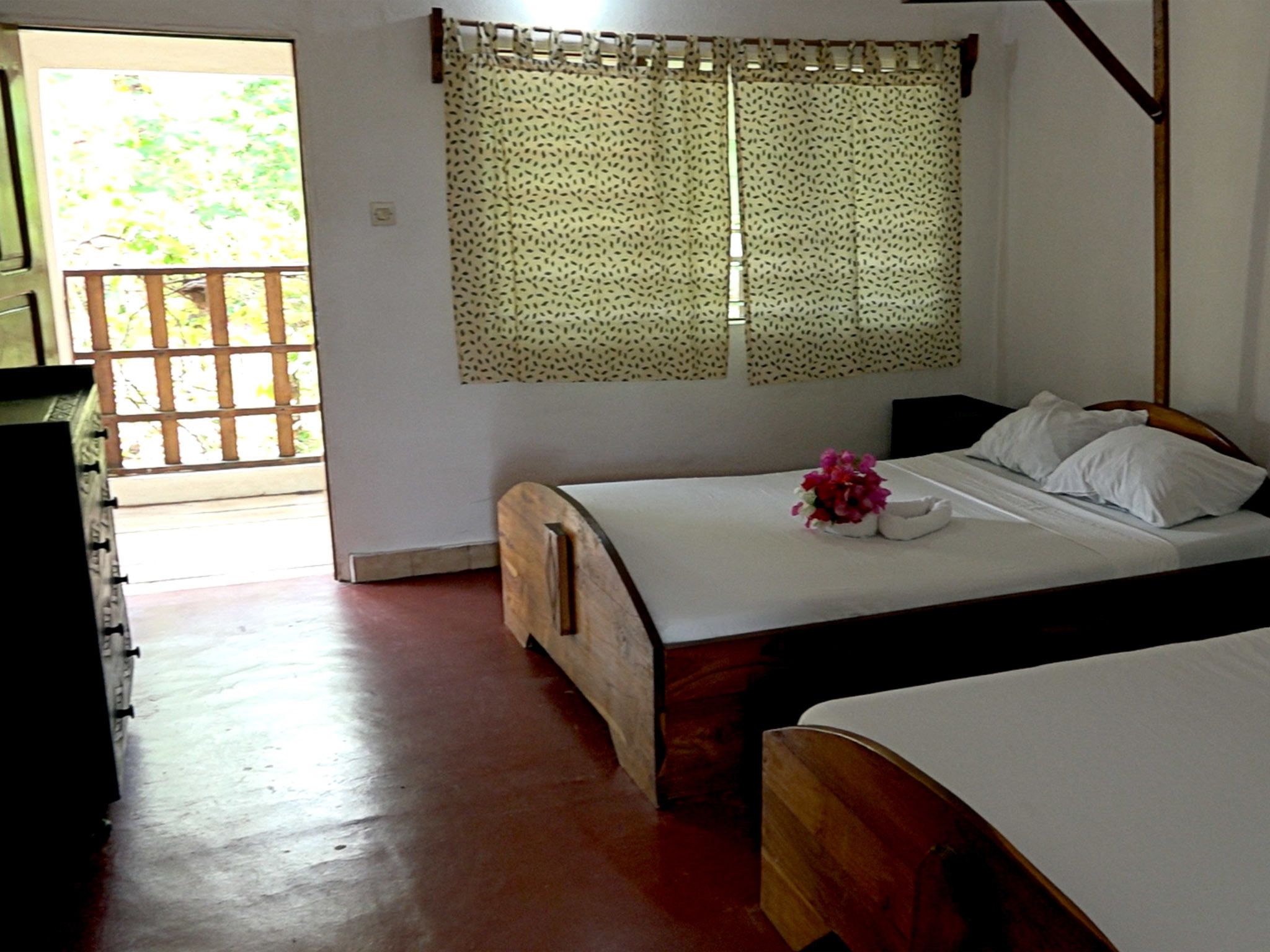 A bedroom with two beds, a wooden headboard, a window with patterned curtains, and a view of the outdoors.