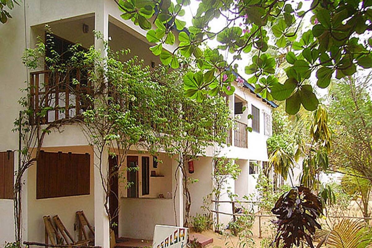 Un edificio de dos pisos con un balcón, rodeado de abundante vegetación.