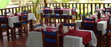 Un restaurante con mesas dispuestas para comer, con vistas a zonas verdes y palmeras.