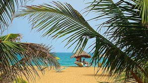 A beach scene with a thatched hut and palm trees. - Hotel Awalé Plage - Village vacances (Grand Popo)