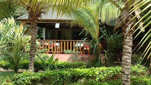 A small, single-story building with a wooden deck and a thatched roof, surrounded by lush tropical vegetation. - Hotel Awalé Plage - Village vacances (Grand Popo)
