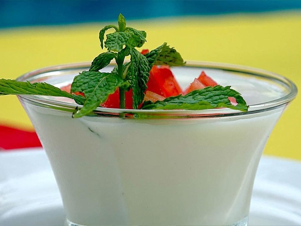 A clear glass dessert with a mint garnish and watermelon pieces.