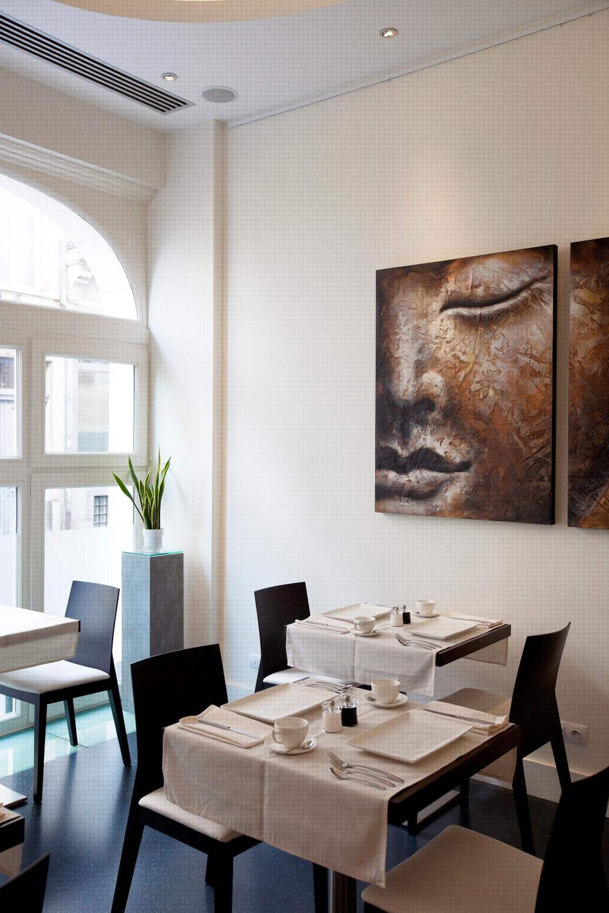 A modern dining area with a table set for two, a potted plant, and abstract artwork on the wall.