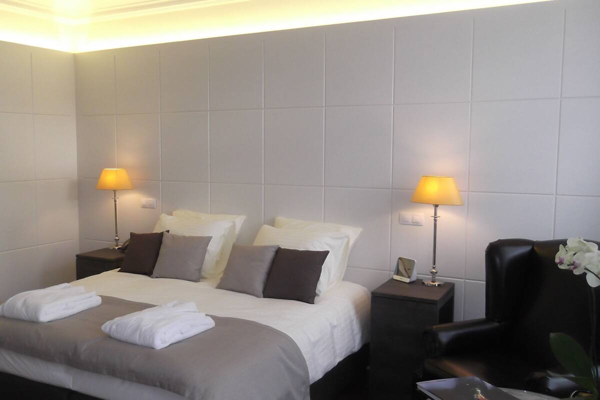 Una habitación de hotel con una cama grande, dos mesitas de noche y dos lámparas.
