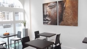 Un comedor moderno con mesas y sillas, una planta en maceta y un cuadro abstracto grande en la pared.