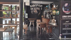 A coffee shop interior with a counter, seating area, and shelves with coffee products. - Dewi Sinta Hotel and Restaurant by ABM (Tabanan)