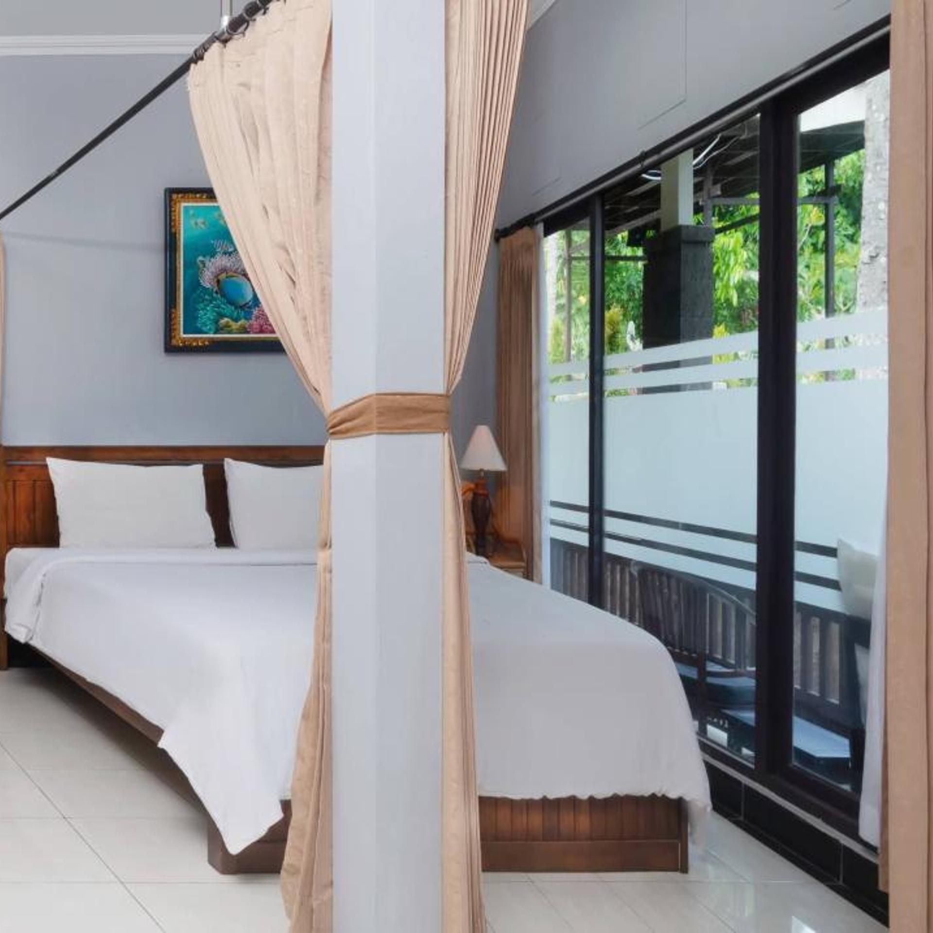 A bedroom with a four-poster bed, a nightstand, a lamp, and a large window with a view of greenery.