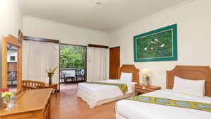 A hotel room with two beds, a dining table, chairs, a balcony with a view of greenery, and a painting on the wall. - Dewi Sinta Hotel and Restaurant by ABM (Tabanan)