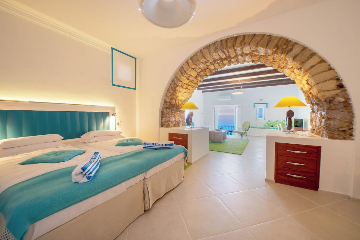 A hotel room with a bed, a desk, a lamp, and an archway leading to another room.