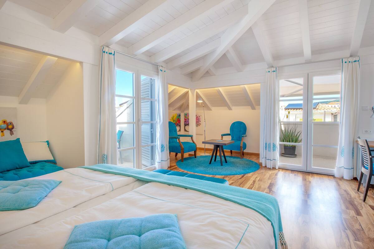 A bedroom with a large bed, a desk, two chairs, and a view of the outside.