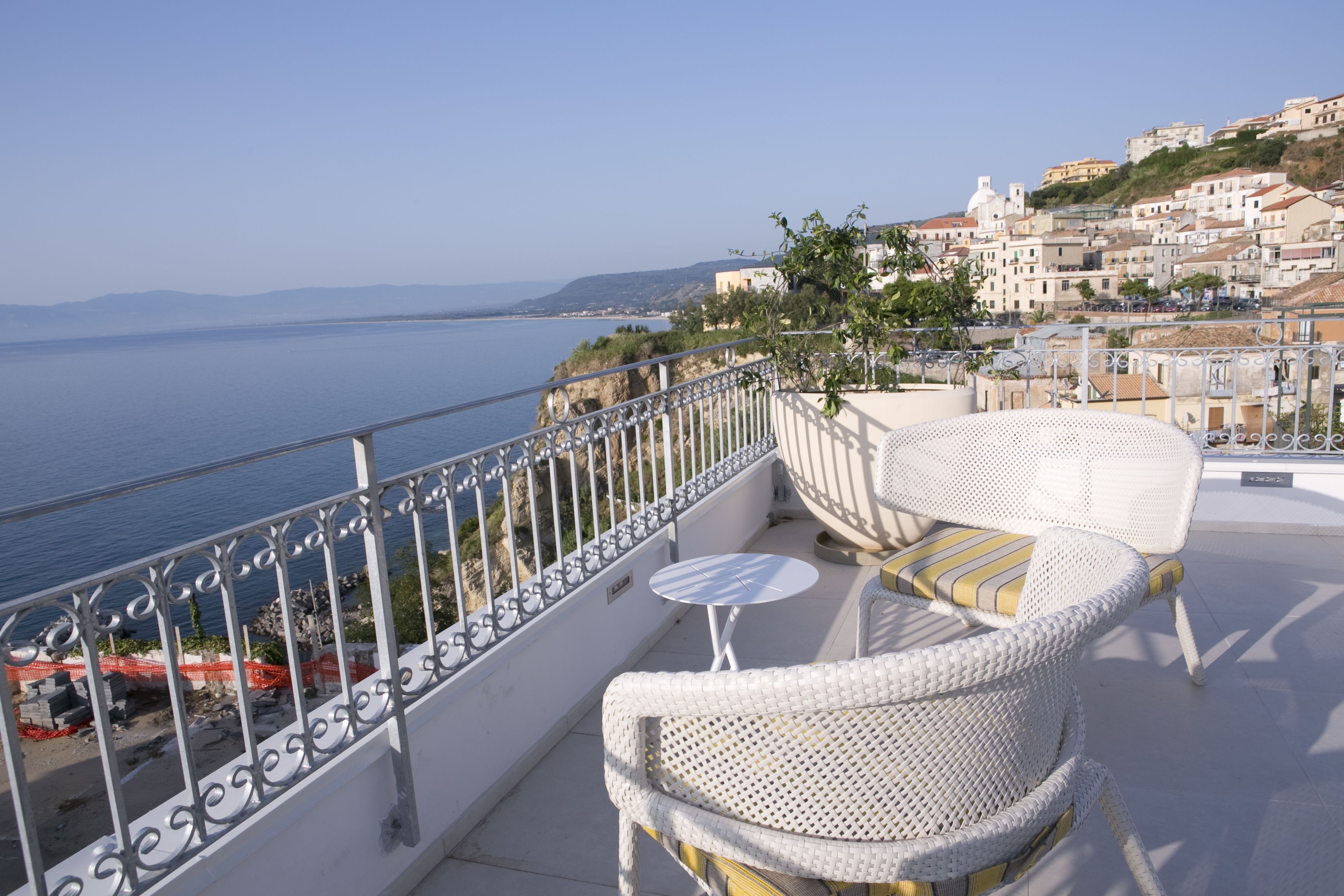 Un balcón con muebles de mimbre y una pequeña mesa, con vistas a un pueblo costero y al mar.