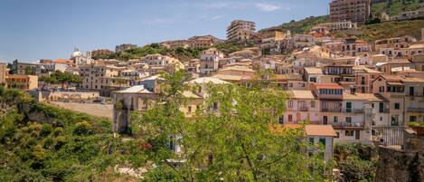 Uma vila pitoresca situada numa encosta íngreme, com edifícios históricos, alguns com cúpulas, e uma igreja imponente com um campanário.