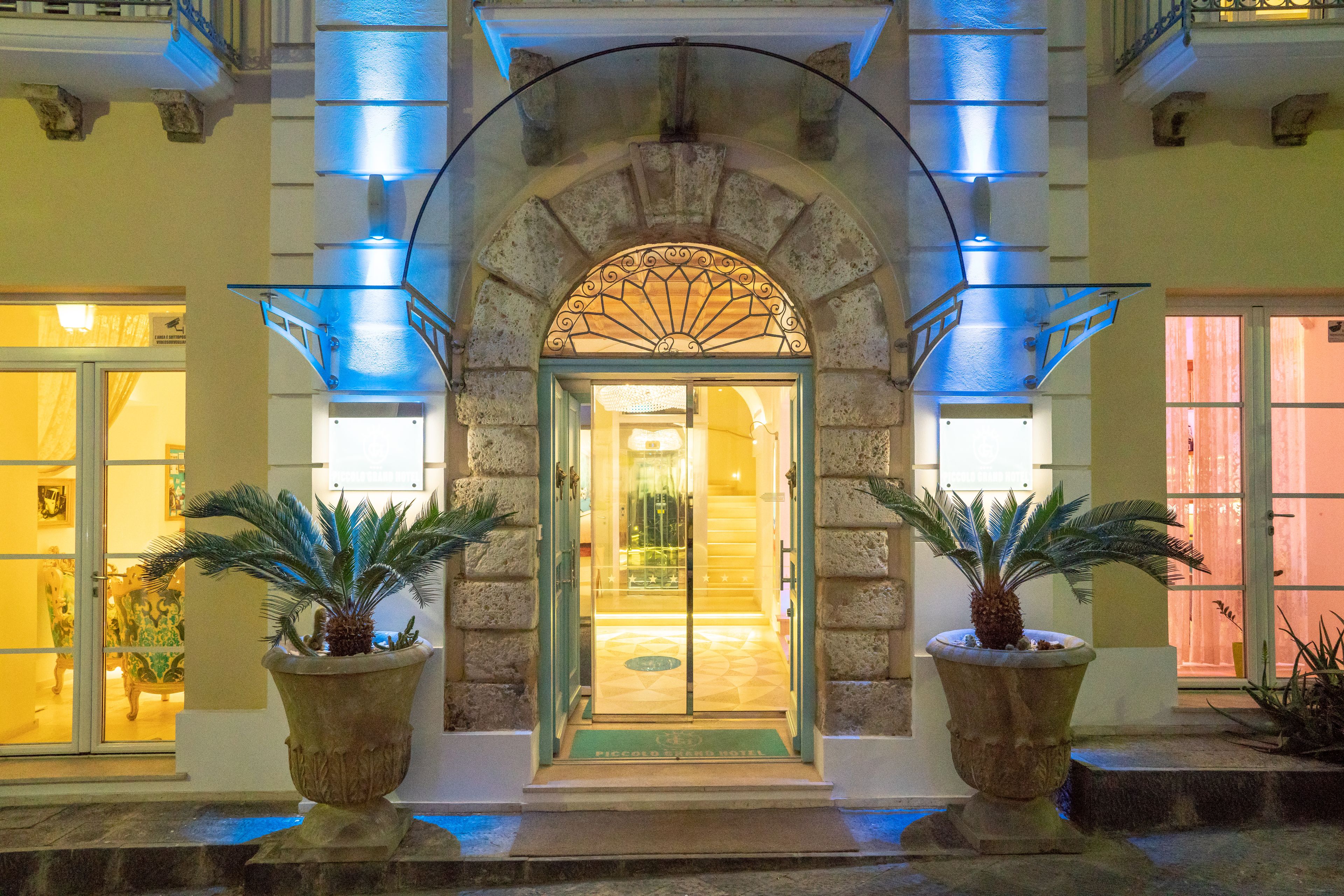 A hotel entrance with a stone archway, glass doors, and potted plants.
