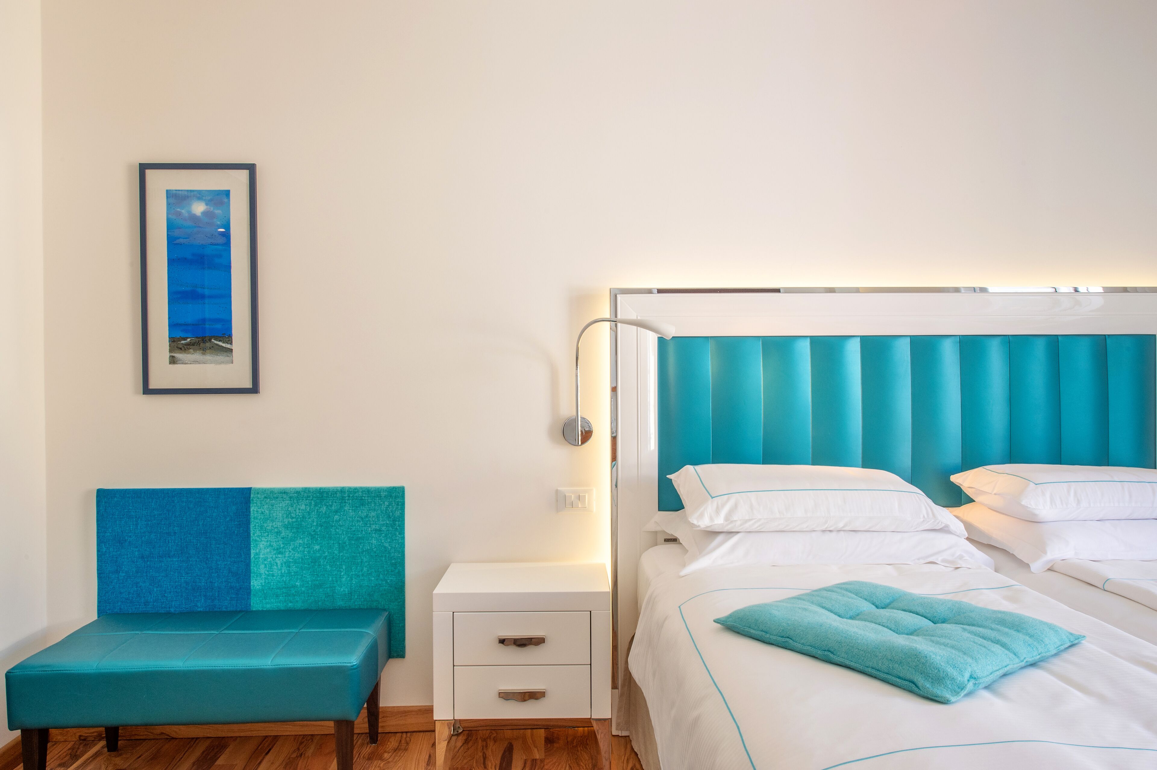 Un dormitorio con cama, mesita de noche, sofá y un cuadro en la pared.