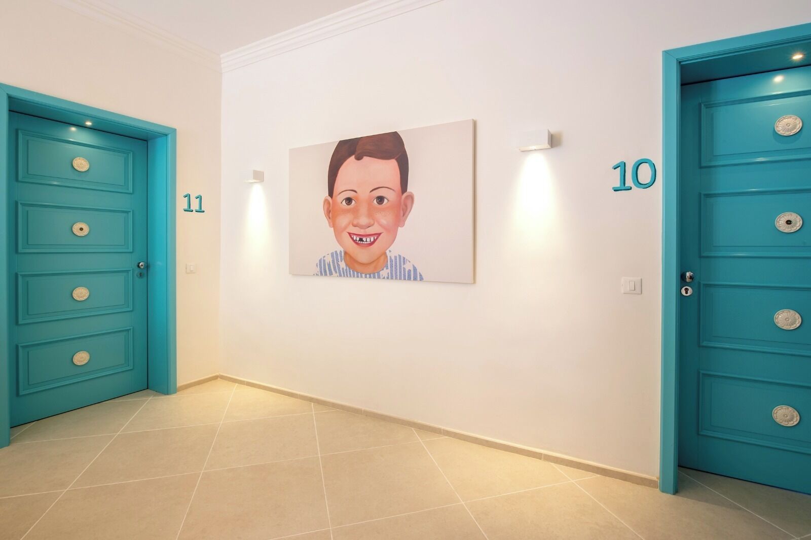 A hallway with teal doors numbered 10 and 11, a tiled floor, and a framed picture on the wall.