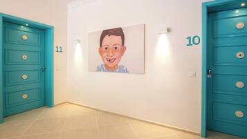 A hallway with teal doors numbered 10 and 11, a tiled floor, and a framed picture on the wall.