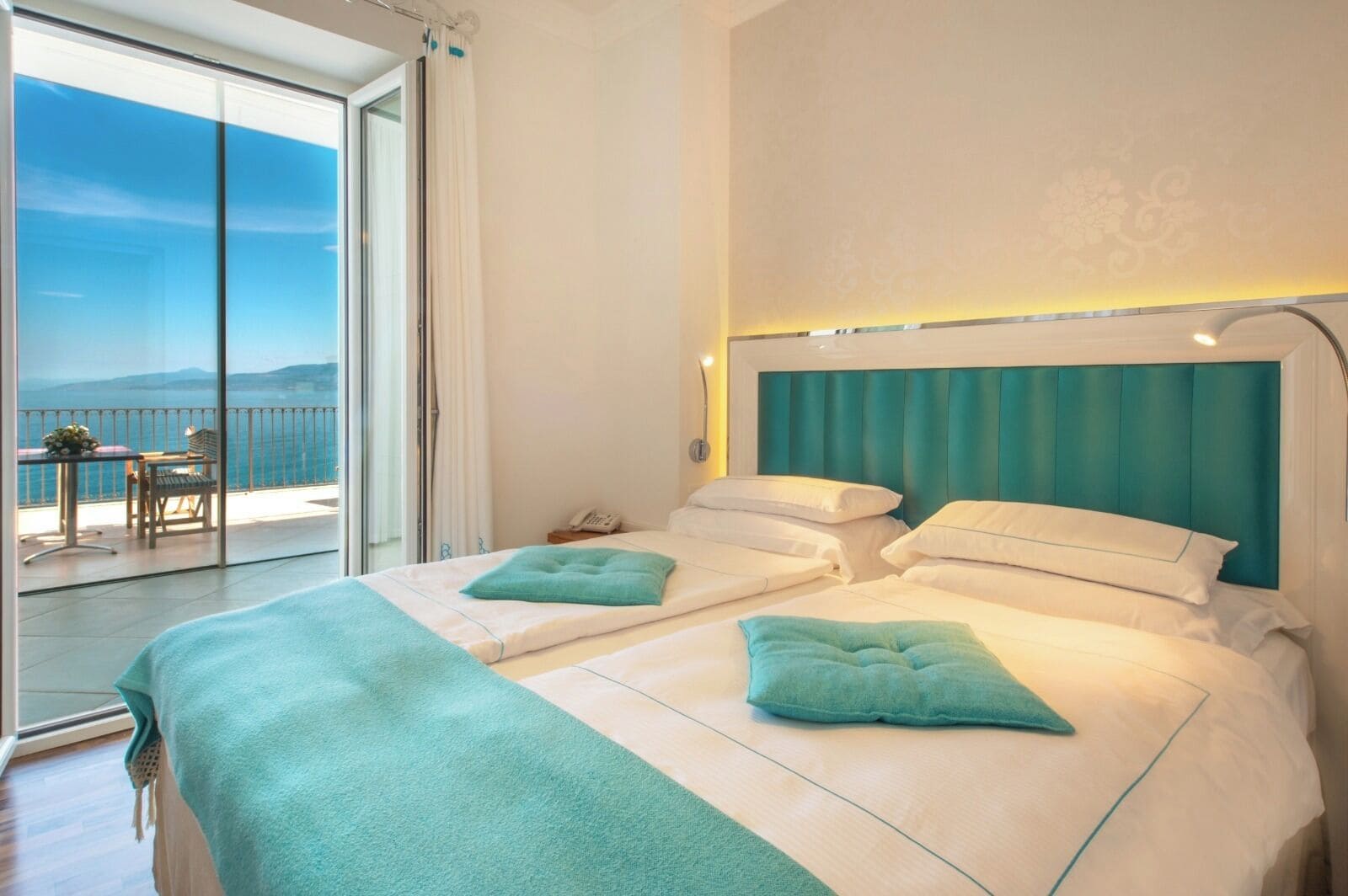 A hotel room with a large bed, a balcony with a view, and a small table with chairs.