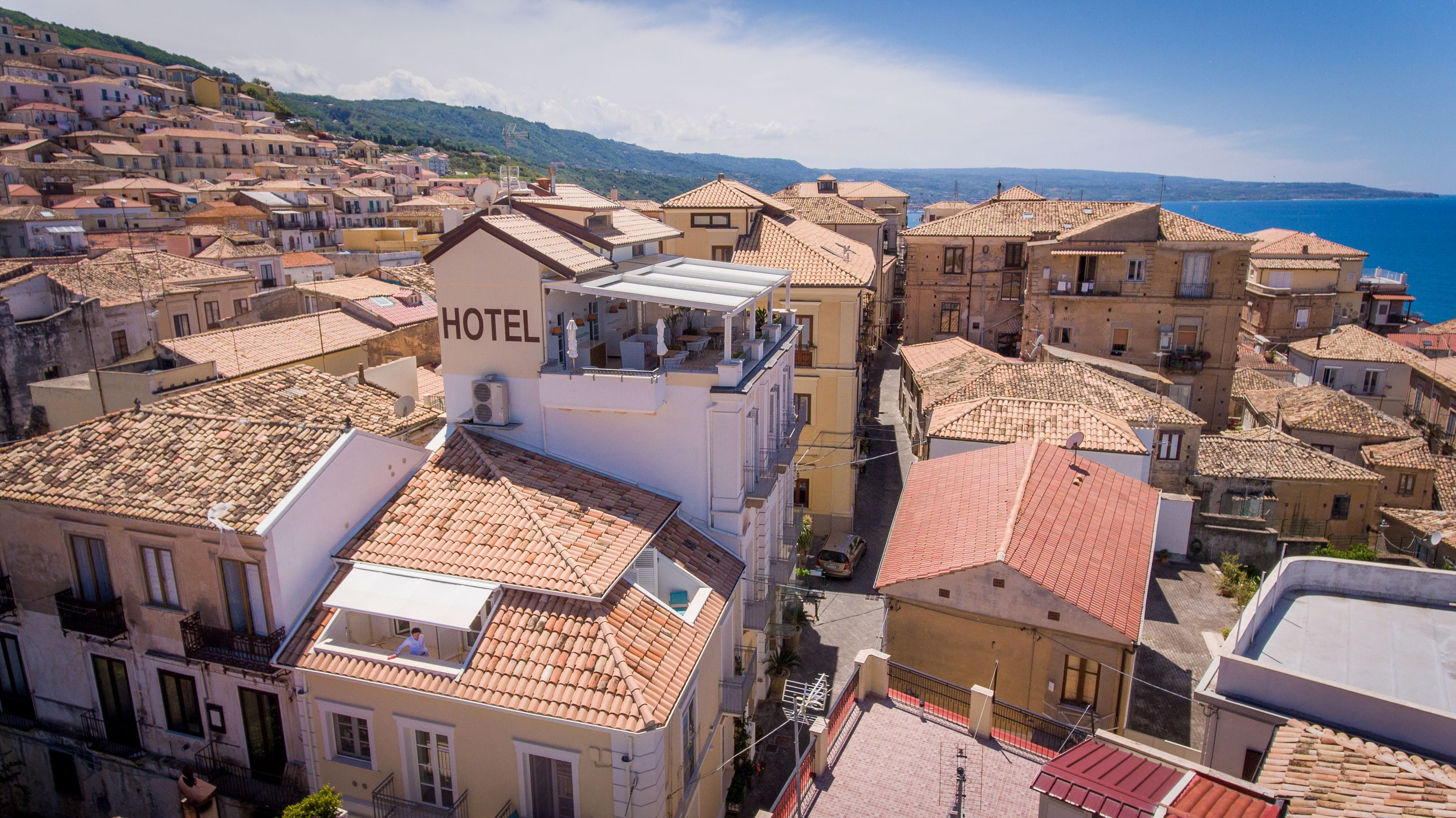 Um hotel com terraço no telhado, rodeado por edifícios tradicionais com telhados de terracota.