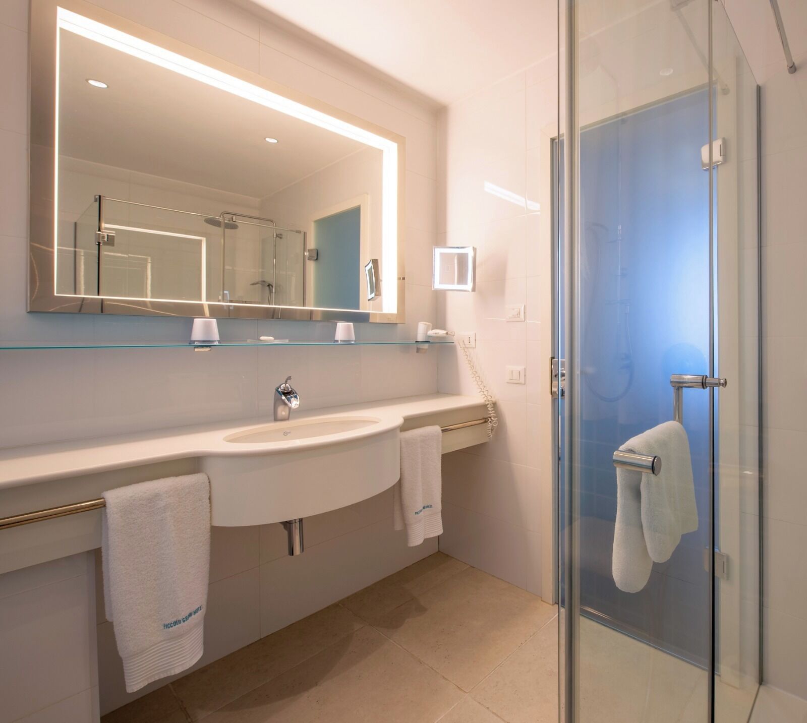 A modern bathroom with a large mirror, a sink, a glass shower enclosure, and two towels.