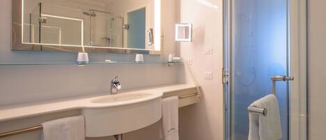 A modern bathroom with a large mirror, a sink, a glass shower enclosure, and two towels.