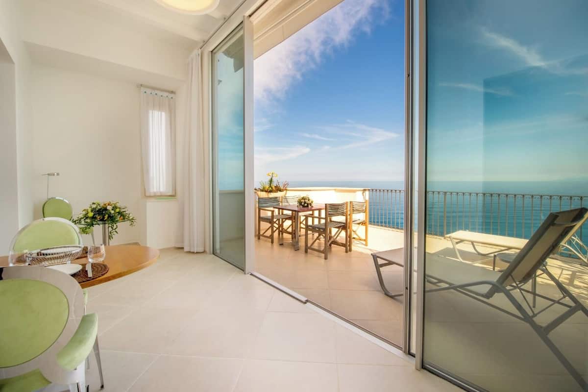 A balcony with a view of the sea, a dining area with chairs and a table, and a sliding glass door.