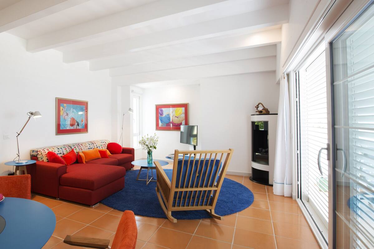A living room with a red sofa, a blue rug, a wooden chair, and a TV.
