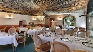 Un ristorante con tavoli rotondi apparecchiati per la cena, con tovaglie bianche e sedie in vimini.