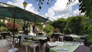 Zona pranzo all'aperto con tavoli e sedie, riparata da ombrelloni e immersa nel verde.
