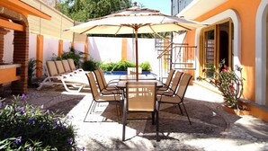 An outdoor patio with a table and chairs, surrounded by plants and a pool.