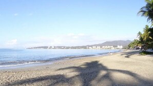 A beach with a clear sky, calm sea, and distant buildings.