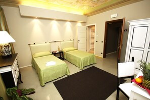 A hotel room with two single beds, a desk with a lamp, a small table, a chair, and a cabinet.