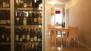 Una bodega con estantes llenos de botellas de vino, un comedor con sillas y una mesa de madera, y un vano que conduce a otra habitación.