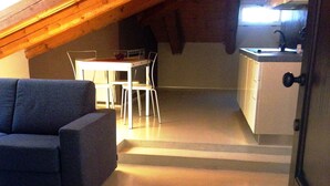 Habitación en el ático con sofá, mesa de comedor, sillas y kitchenette.
