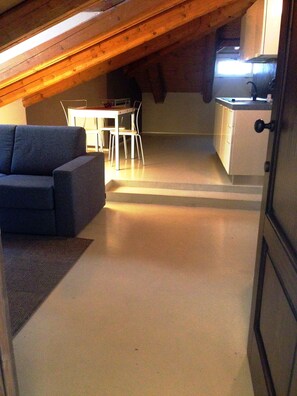 Habitación en el ático con sofá, mesa de comedor, sillas y kitchenette.