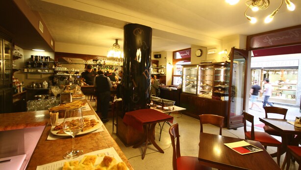 Un interior de restaurante con barra, mesas y sillas de madera.