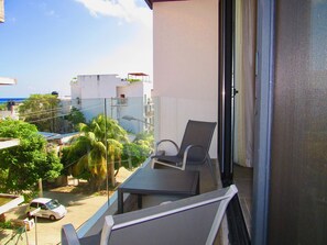 A balcony with a table and chairs, overlooking a street with buildings and trees. - Condo Soul by Playa Paradise (Playa del Carmen)