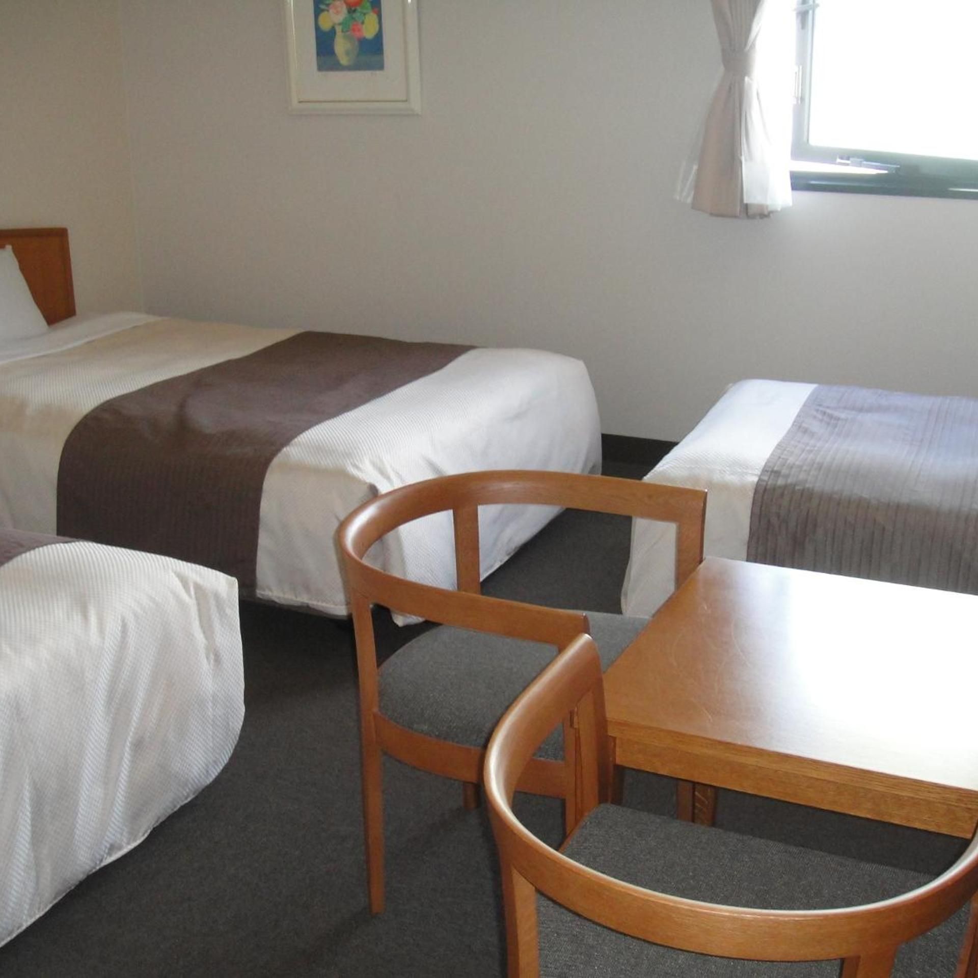 A hotel room with two beds, a wooden chair, and a table.