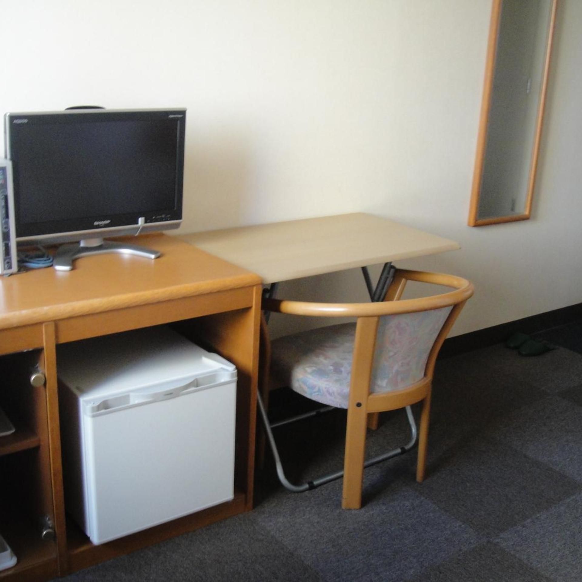 A compact workspace with a desk, a chair, a small refrigerator, and a computer monitor.